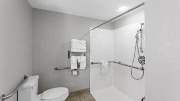 Un baño moderno con inodoro, ducha con barras de apoyo y toallero con toallas dobladas.