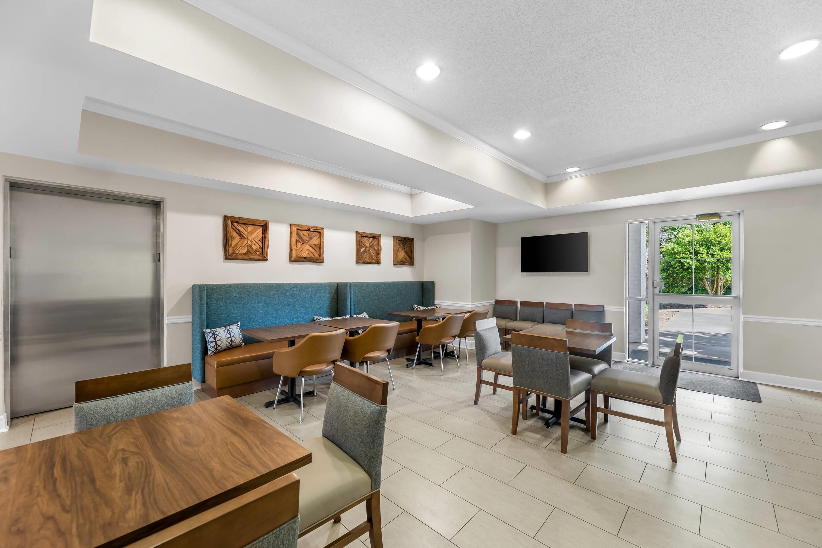 A modern dining area with wooden tables and chairs, a blue cushioned bench, and a flat-screen TV mounted on the wall.
