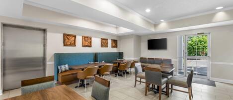 A modern dining area with wooden tables and chairs, a blue cushioned bench, and a flat-screen TV mounted on the wall.