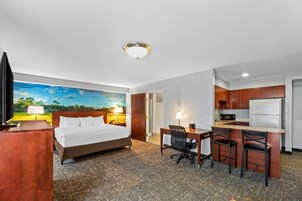 Une chambre d’hôtel équipée d’un lit, d’un bureau, de chaises, d’une kitchenette et ornée d’un tableau au mur.
