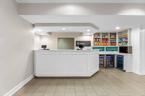 A reception area with a white reception desk, a glass door, a sign for 'Claron Ponte by Clopack Hotel,' and a snack bar with various packaged goods. - Starkville Inn and Suites (Starkville)