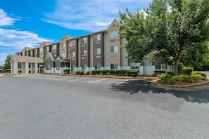 A multi-story hotel with a parking lot and a flag. - Starkville Inn and Suites (Starkville)
