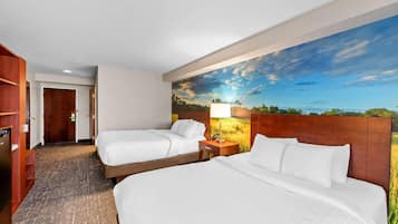 Habitación de hotel con dos camas, cabecero de madera, mesita de noche con lámpara y un mural grande con un paisaje en la pared.