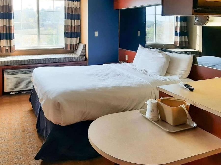 Een hotelkamer met een bed, nachtkastje en een raam met gordijnen.