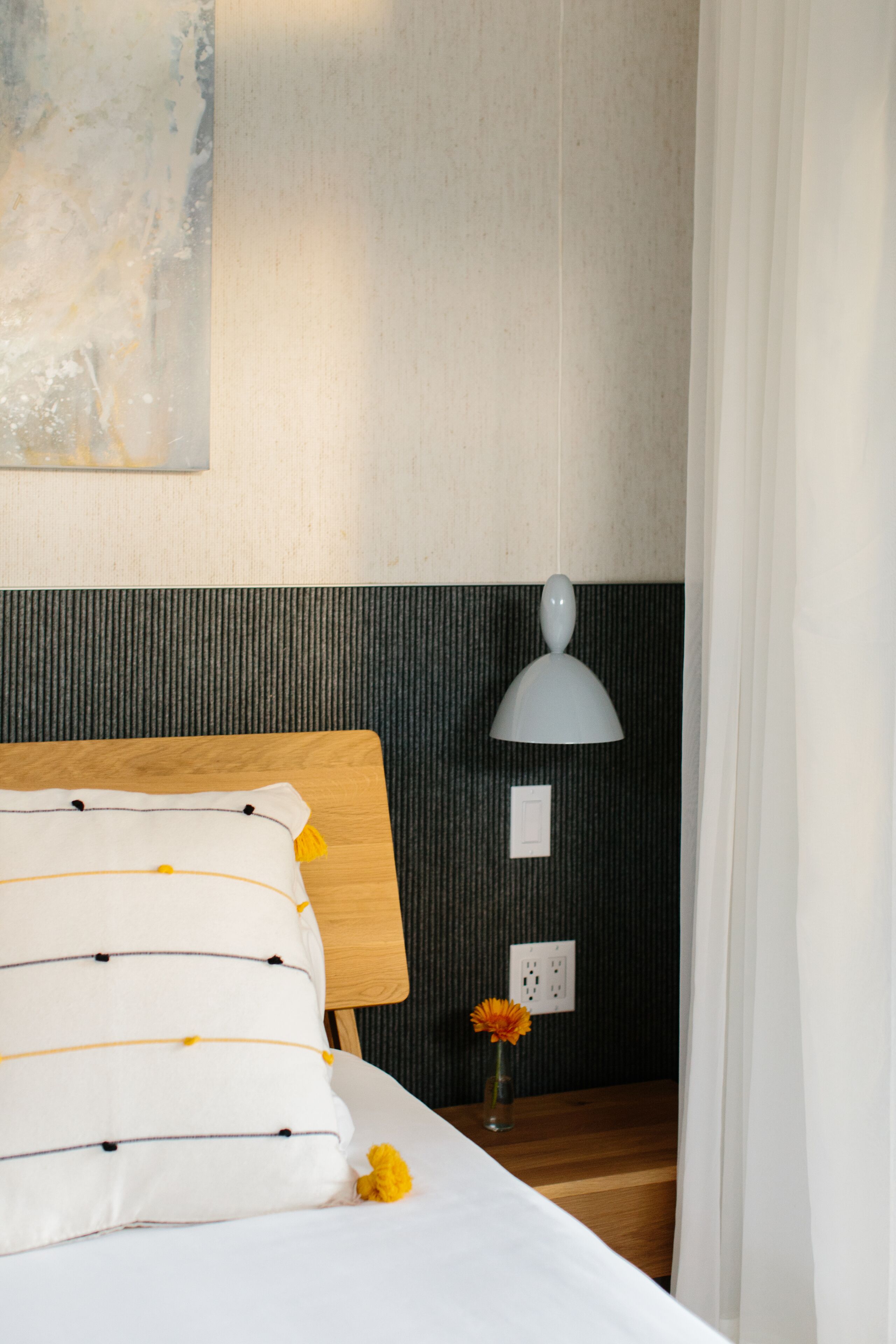 Un letto rifatto con lenzuola bianche e cuscini a righe, un comodino con una lampada e una presa elettrica a parete.