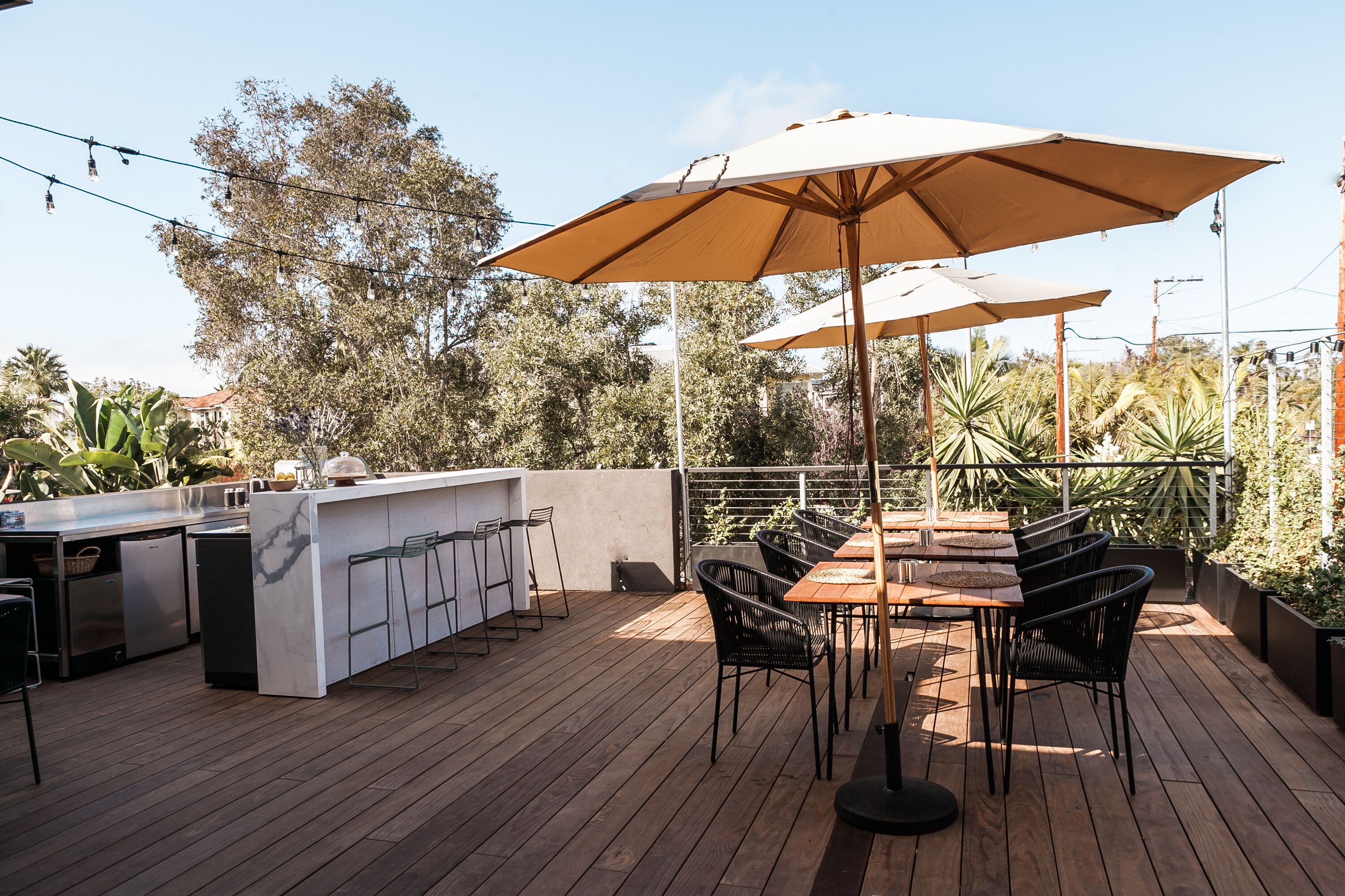 An outdoor patio with a wooden deck, a bar area with stools, and a table with chairs under a large umbrella.