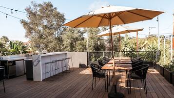 An outdoor patio with a wooden deck, a bar area with stools, and a table with chairs under a large umbrella.