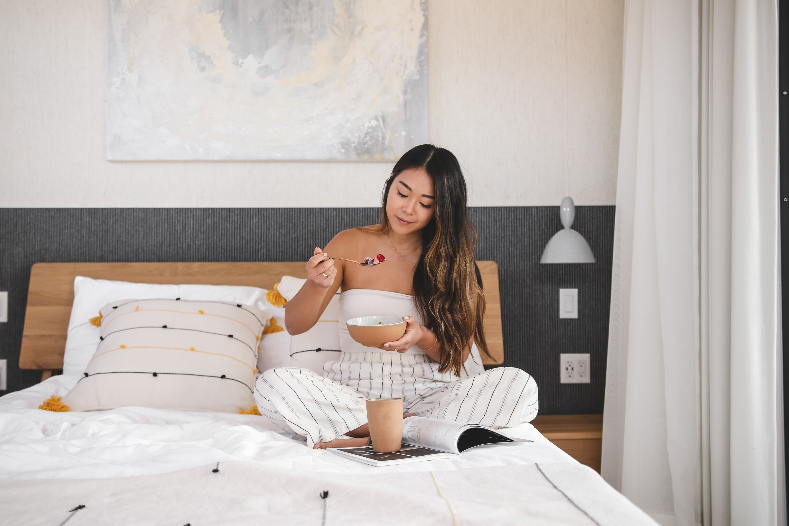 Una persona sentada en una cama con un libro, un tazón y una cuchara.