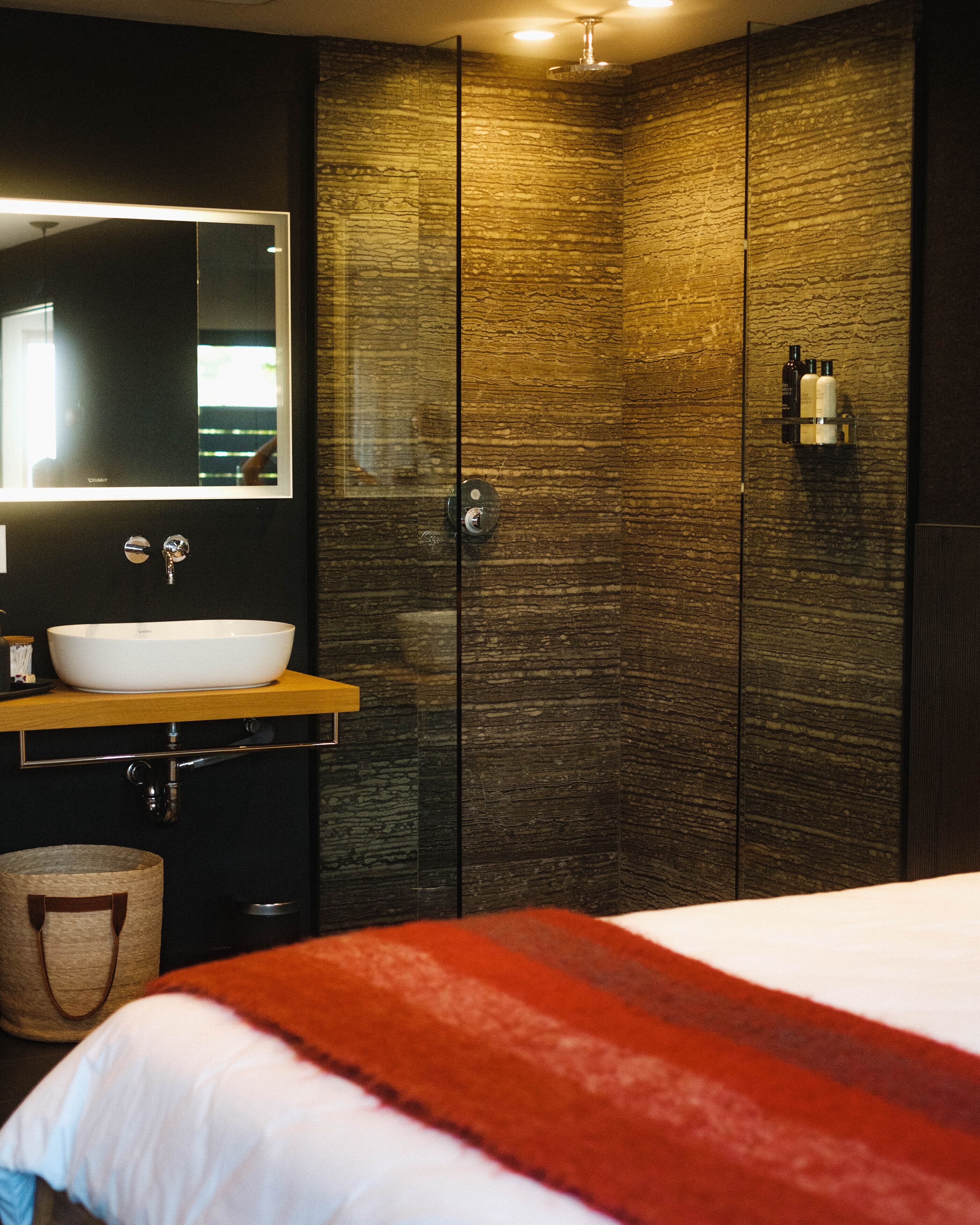 Un baño moderno con un espejo grande, un lavamanos blanco y una pared de madera con textura.