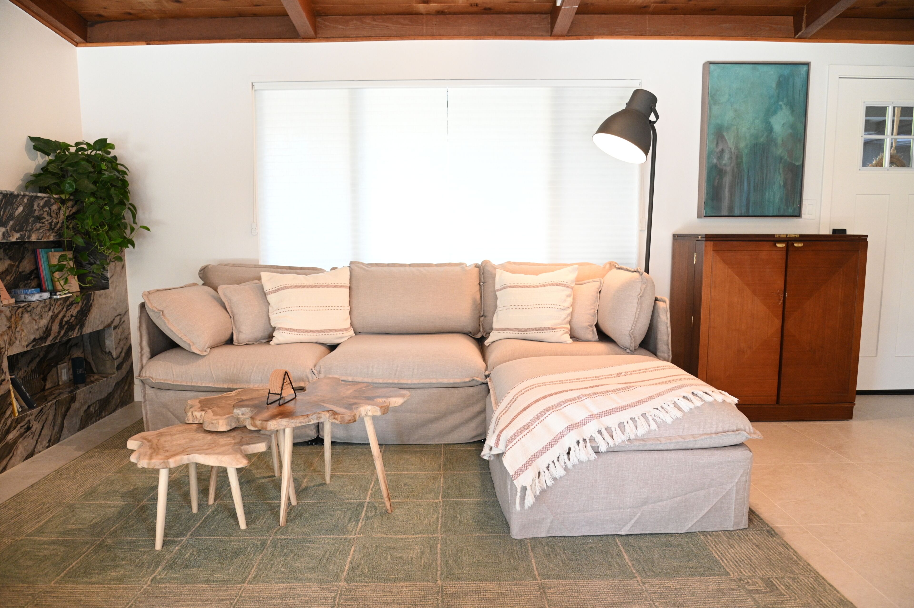 Una sala de estar con sofá, un aparador de madera, una lámpara de pie y una planta.