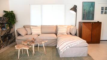 Una sala de estar con sofá, un aparador de madera, una lámpara de pie y una planta.
