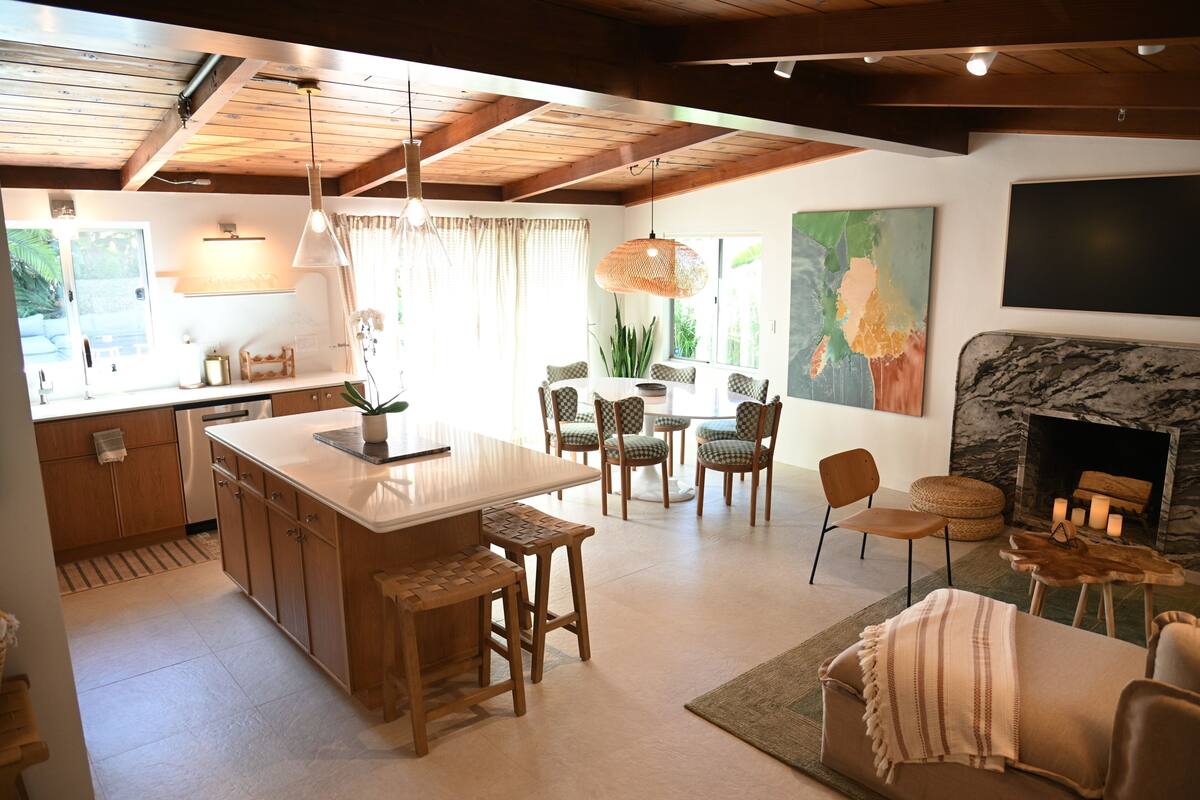 A modern kitchen with wooden cabinets, a central island, bar stools, and a dining area with chairs.