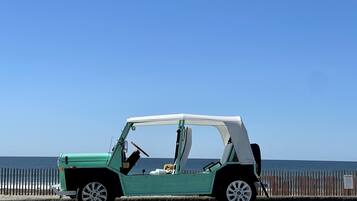 A teal convertible car parked on a road with a view of the ocean.
