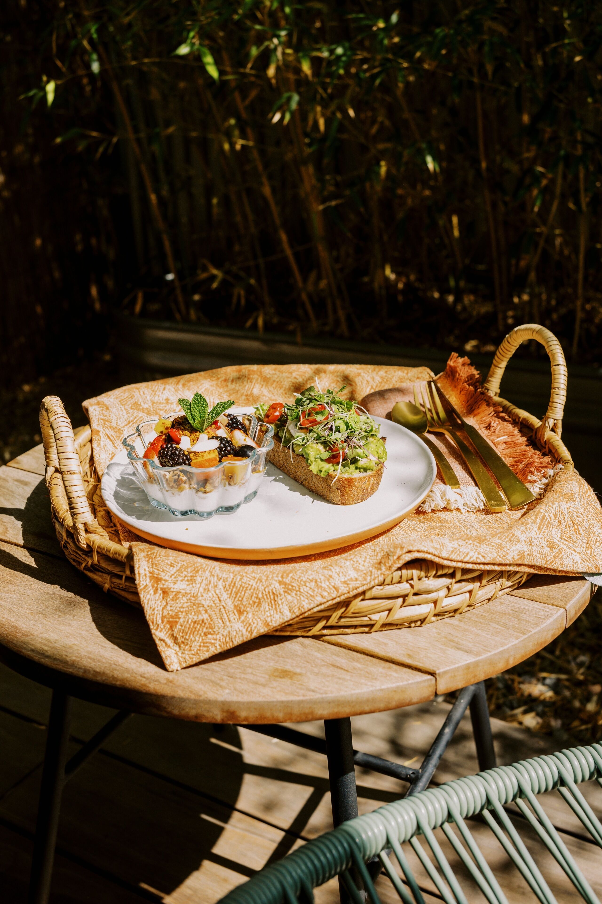Ein runder Holztisch mit einem gewebten Korb, einer Speisenplatte und einer kleinen Salatschüssel.