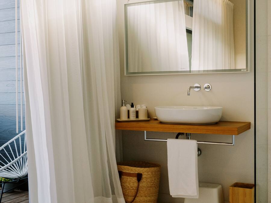 A modern bathroom with a large mirror, a white sink, and a wooden vanity.