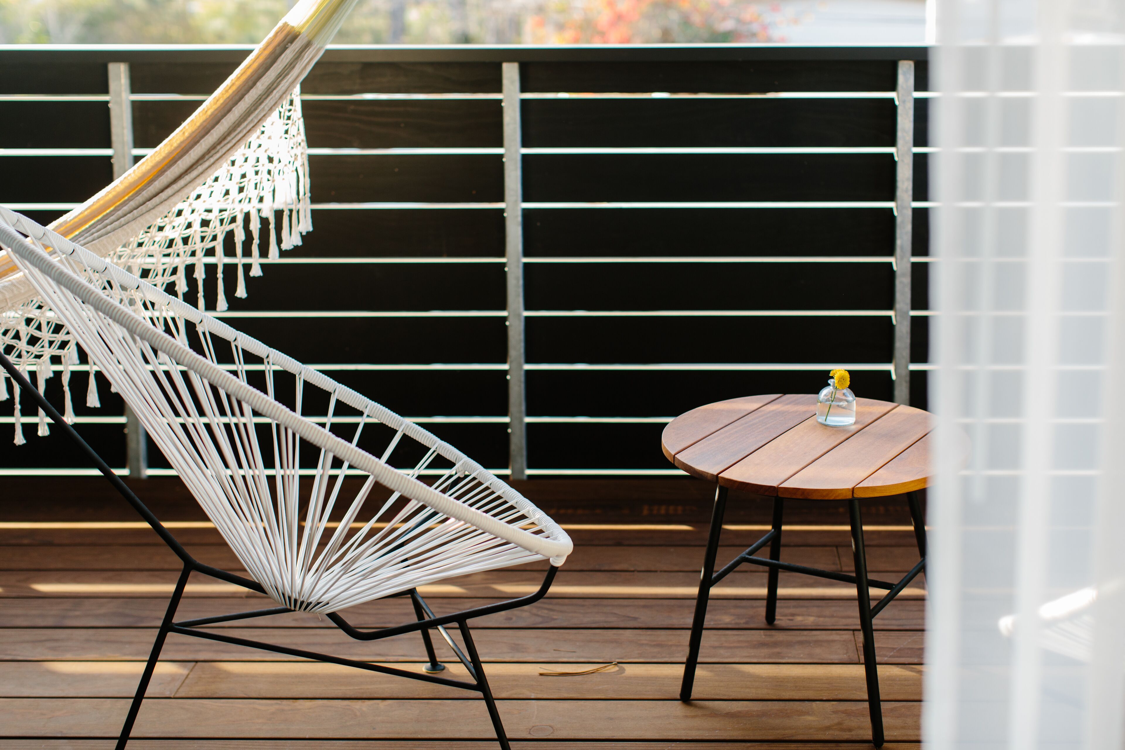 A hammock chair and a small round table on a wooden deck.