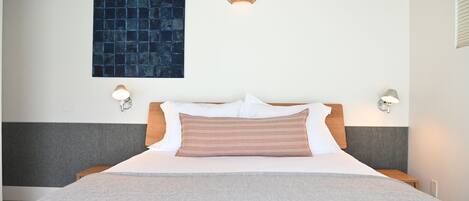 Une chambre d’hôtel avec un lit, deux lampes de chevet, un luminaire fixé au mur et une œuvre d’art bleue à texture.