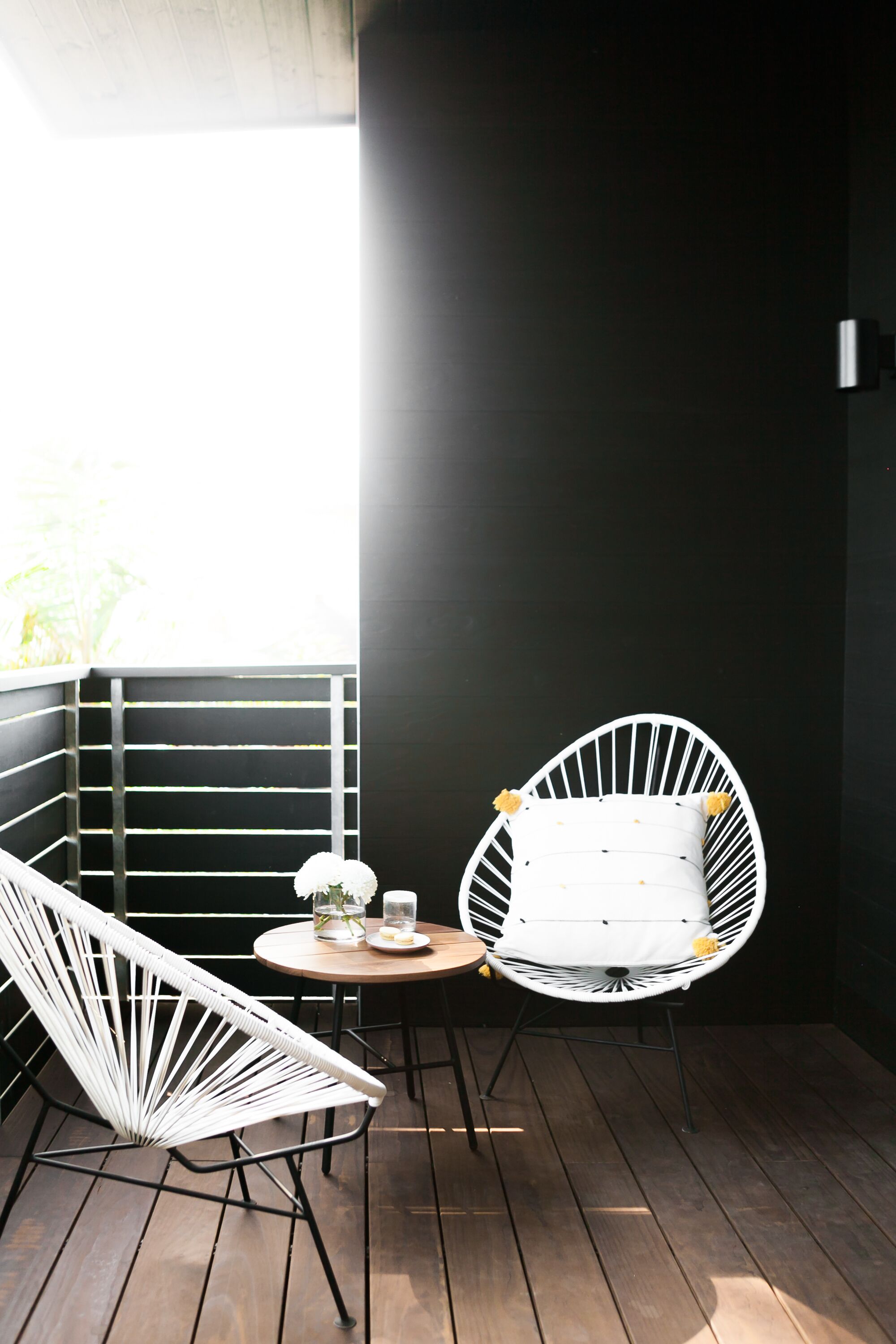 Un petit espace extérieur aménagé avec des sièges, délimité et abrité, comprenant deux chaises blanches et une table ronde, offrant une vue à travers une fenêtre.