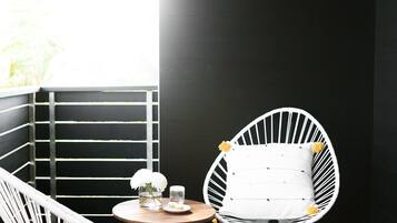 Un petit espace extérieur aménagé avec des sièges, délimité et abrité, comprenant deux chaises blanches et une table ronde, offrant une vue à travers une fenêtre.