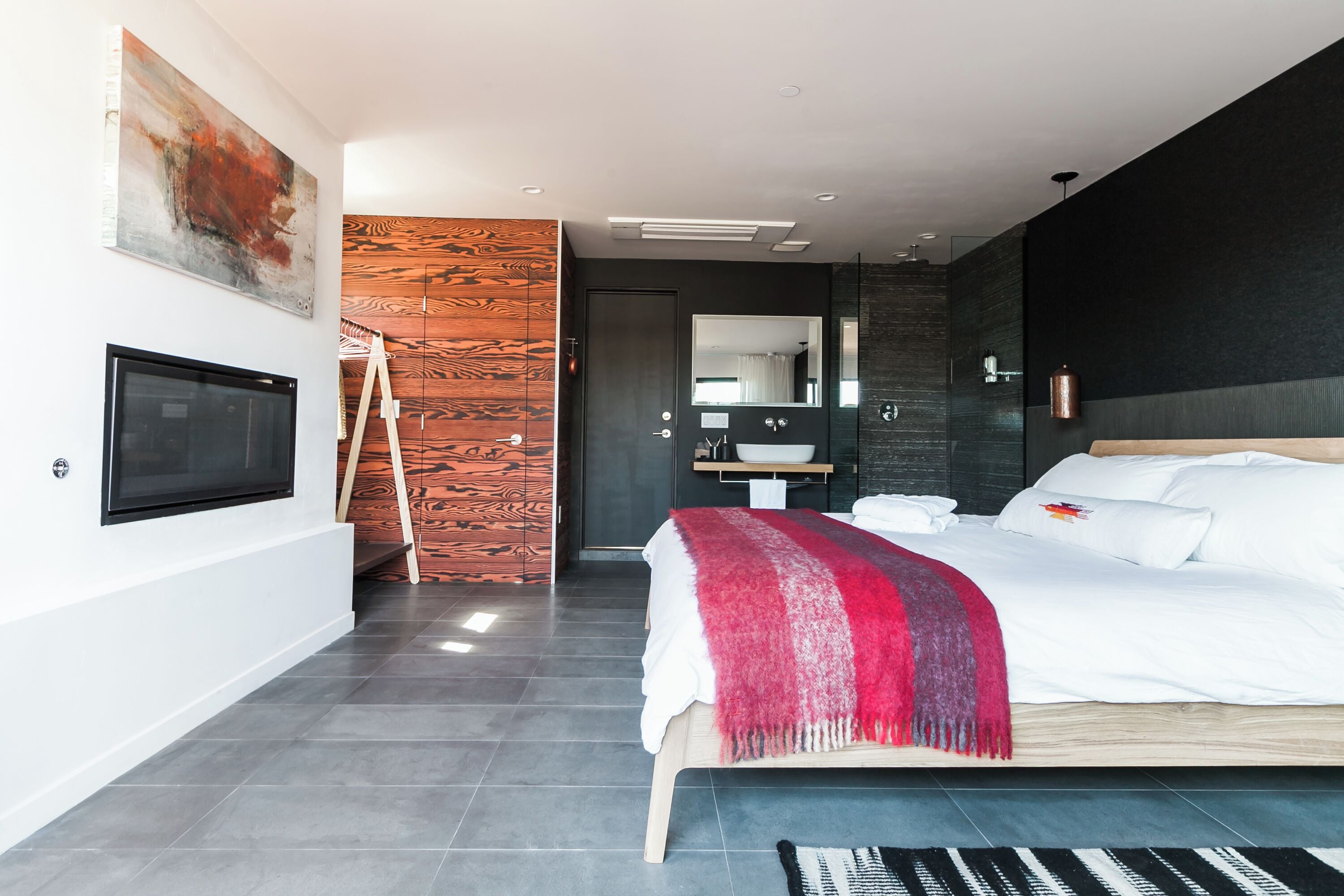 Un dormitorio moderno con una cama grande, un televisor, una pared de acento de madera, un baño con espejo y un cuadro en la pared.