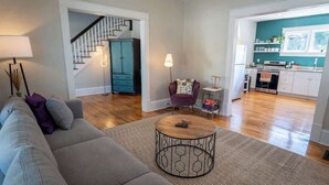 A spacious living room with a sofa, a coffee table, and a staircase leading to a kitchen area. - Stay Roanoke | Downtown Home + Greenway Access (Roanoke)