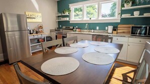 A modern kitchen with white cabinets, a stainless steel refrigerator, and a dining table with placemats. - Stay Roanoke | Downtown Home + Greenway Access (Roanoke)
