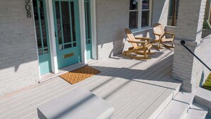A porch with wooden chairs and a bench, a teal door, and a white brick wall. - Stay Roanoke | Downtown Home + Greenway Access (Roanoke)