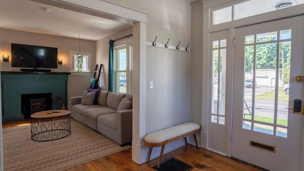 A living room with a sofa, a TV, a fireplace, and a bench near the door. - Stay Roanoke | Downtown Home + Greenway Access (Roanoke)
