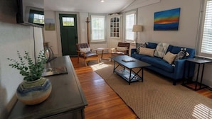 A cozy living room with a blue sofa, two armchairs, a coffee table, and a TV mounted on the wall. - Stay Roanoke | Rustic Cabin Near McAfee Knob (Catawba)