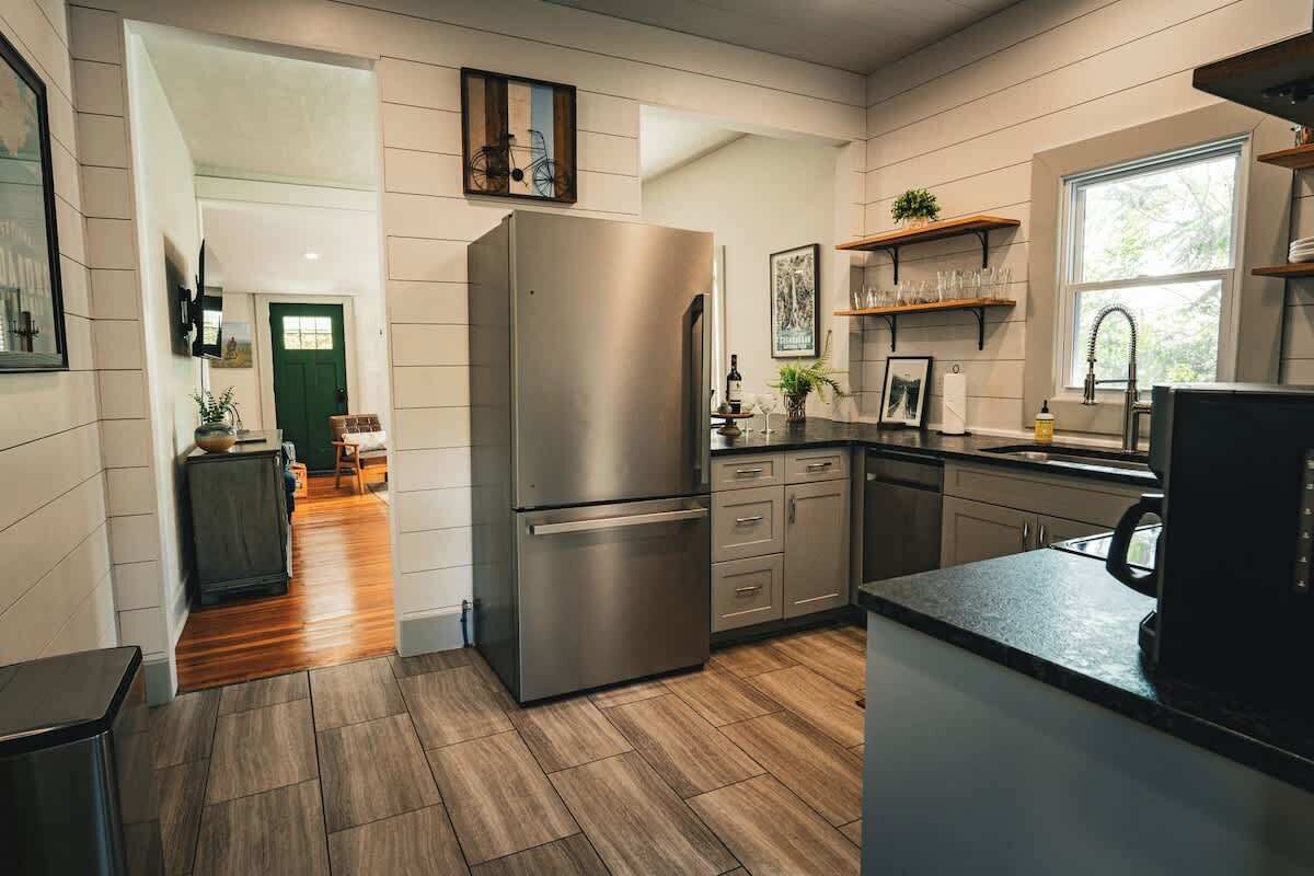 A modern kitchen with a stainless steel refrigerator, wooden flooring, and built-in cabinetry.