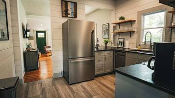 A modern kitchen with a stainless steel refrigerator, wooden flooring, and built-in cabinetry.