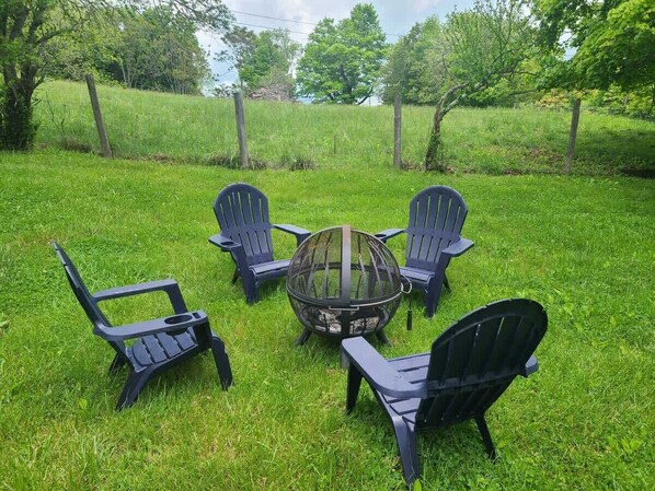 Un foyer est entouré de quatre chaises Adirondack dans un espace extérieur verdoyant.