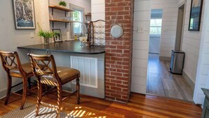 A kitchen with wooden cabinets, a brick accent wall, and a dining area with two wooden chairs. - Stay Roanoke | Rustic Cabin Near McAfee Knob (Catawba)
