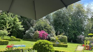 En välskött trädgård med prydligt klippta häckar, ett stort utbud av blommande växter och några få sittplatser utomhus.