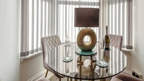 Une table ronde en verre, avec une lampe au centre, deux chaises et une bouteille de vin.