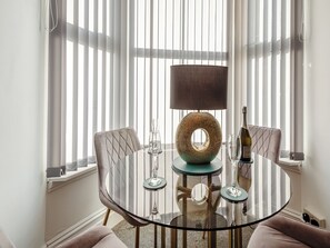A round glass table with a central lamp, two chairs, and a bottle of wine.
