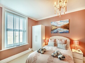A bedroom with a bed, bedside lamps, a wardrobe, a window with blinds, and a painting on the wall.