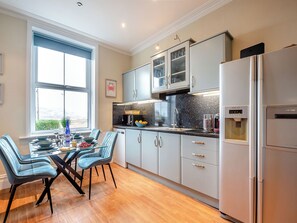 A modern kitchen with a dining area, featuring a large window, stainless steel appliances, and light-colored cabinetry.
