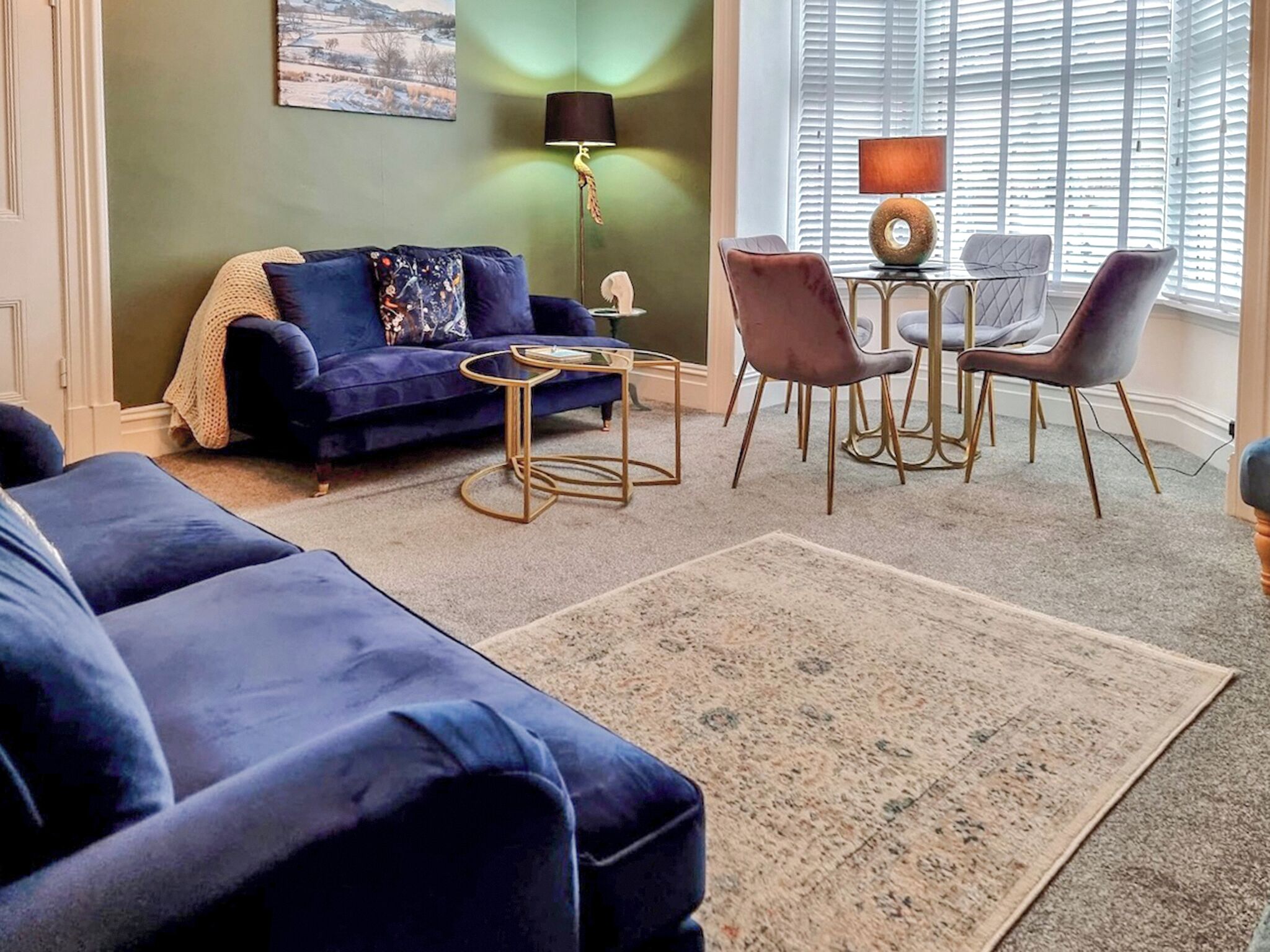 A living room with a blue sofa, a coffee table, and a dining area with chairs and a lamp.