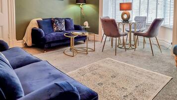 A living room with a blue sofa, a coffee table, and a dining area with chairs and a lamp.