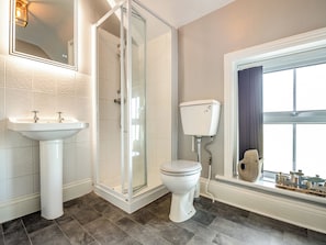 A bathroom with a glass-enclosed shower, a pedestal sink, a toilet, and a window with a view.