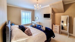 Une chambre à coucher avec un lit, une commode, une télévision, un miroir et un lustre.