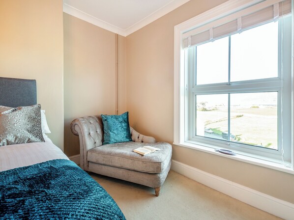 A bedroom with a bed, a chair, a window, and a view of the outdoors.
