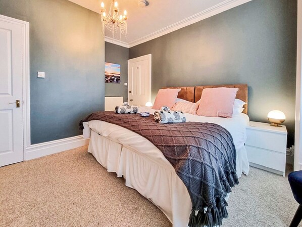 A bedroom with a bed, nightstands, a chandelier, and a painting on the wall.