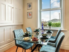 A dining area with a glass table, blue upholstered chairs, and a view of the outdoors through a large window.