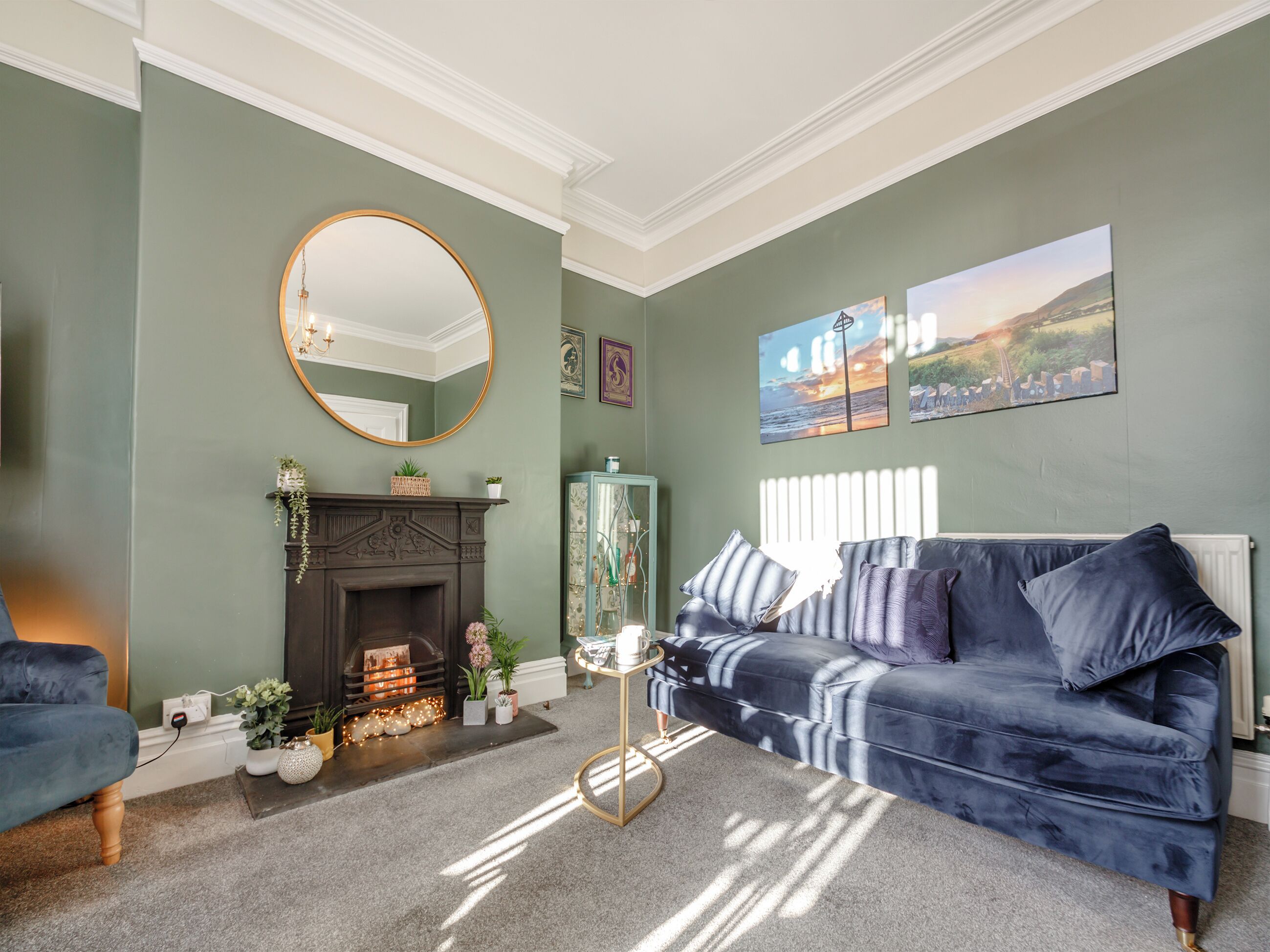 A living room with a fireplace, a blue sofa, a round mirror, and framed artwork on the wall.