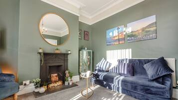 A living room with a fireplace, a blue sofa, a round mirror, and framed artwork on the wall.