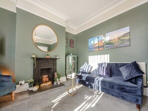 A living room with a fireplace, a blue sofa, a round mirror, and framed artwork on the wall.
