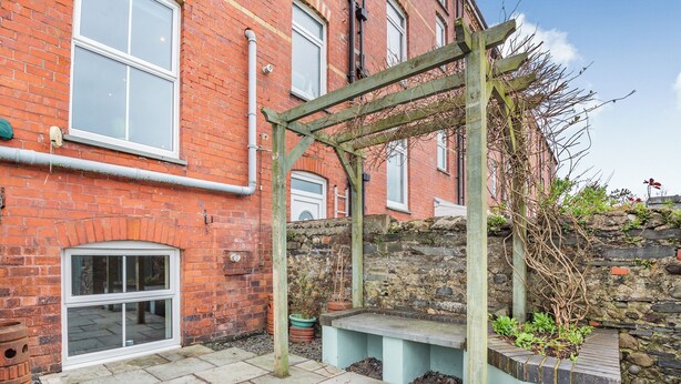 Un bâtiment en briques avec un mur en pierre, une pergola en bois et un banc en pierre.