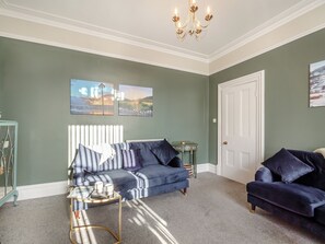 A living room with a blue sofa, a small side table, a chandelier, and two framed pictures on the wall.
